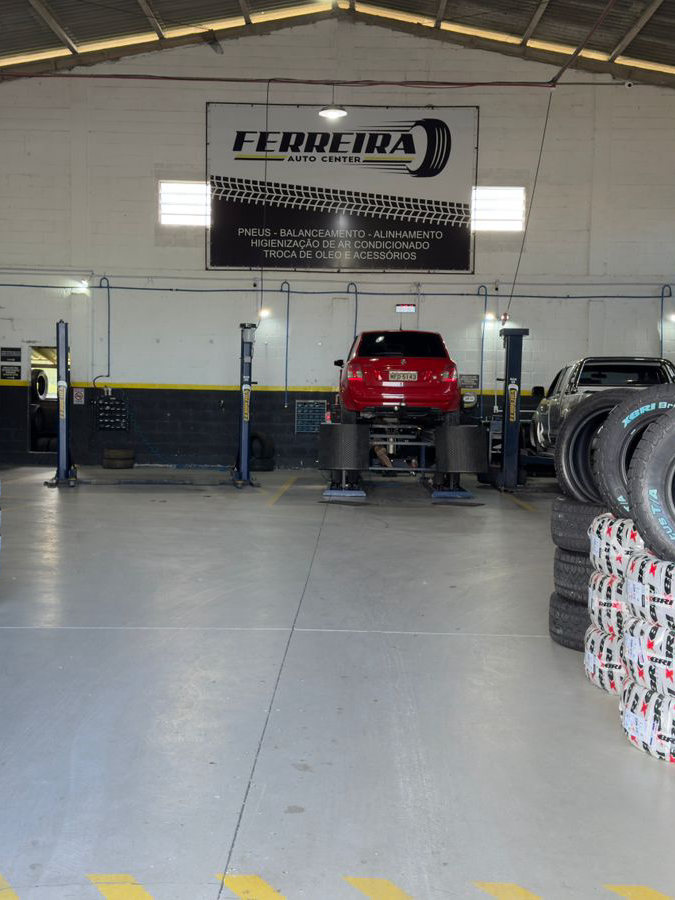 Salão da oficina da Ferreira Auto Center, com a placa da empresa na parede do fundo e pneus dos dois lados